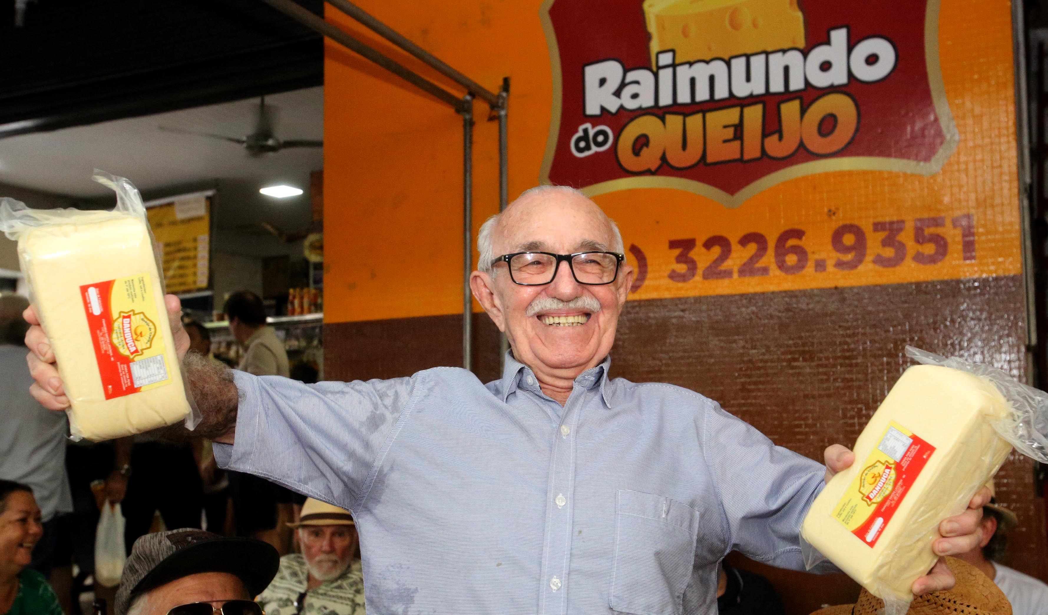 senhor idoso sorrindo para a foto e segurando dois pedaços de queijos